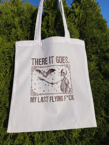 White tote bag with graphic design and text against a green tree background