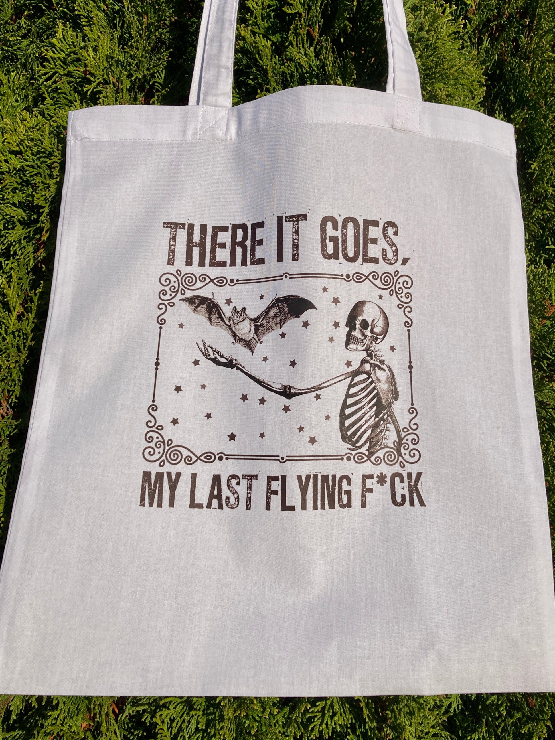 White tote bag with skeleton and bat design and text on a green background