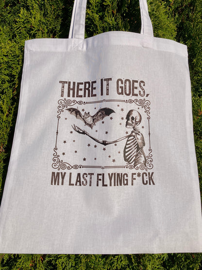 White tote bag with skeleton and bat design and text on a green background