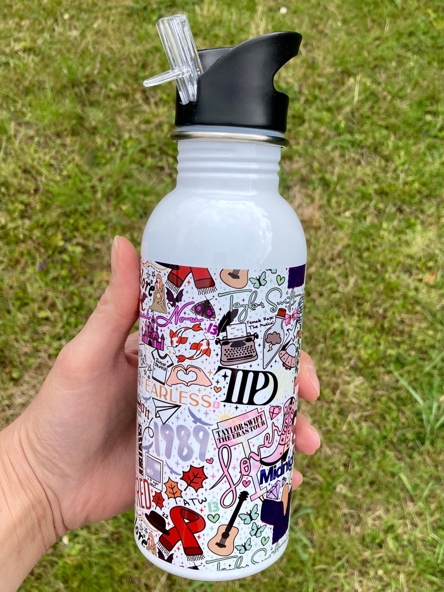 White water bottle with colorful designs held in a hand against a grassy background