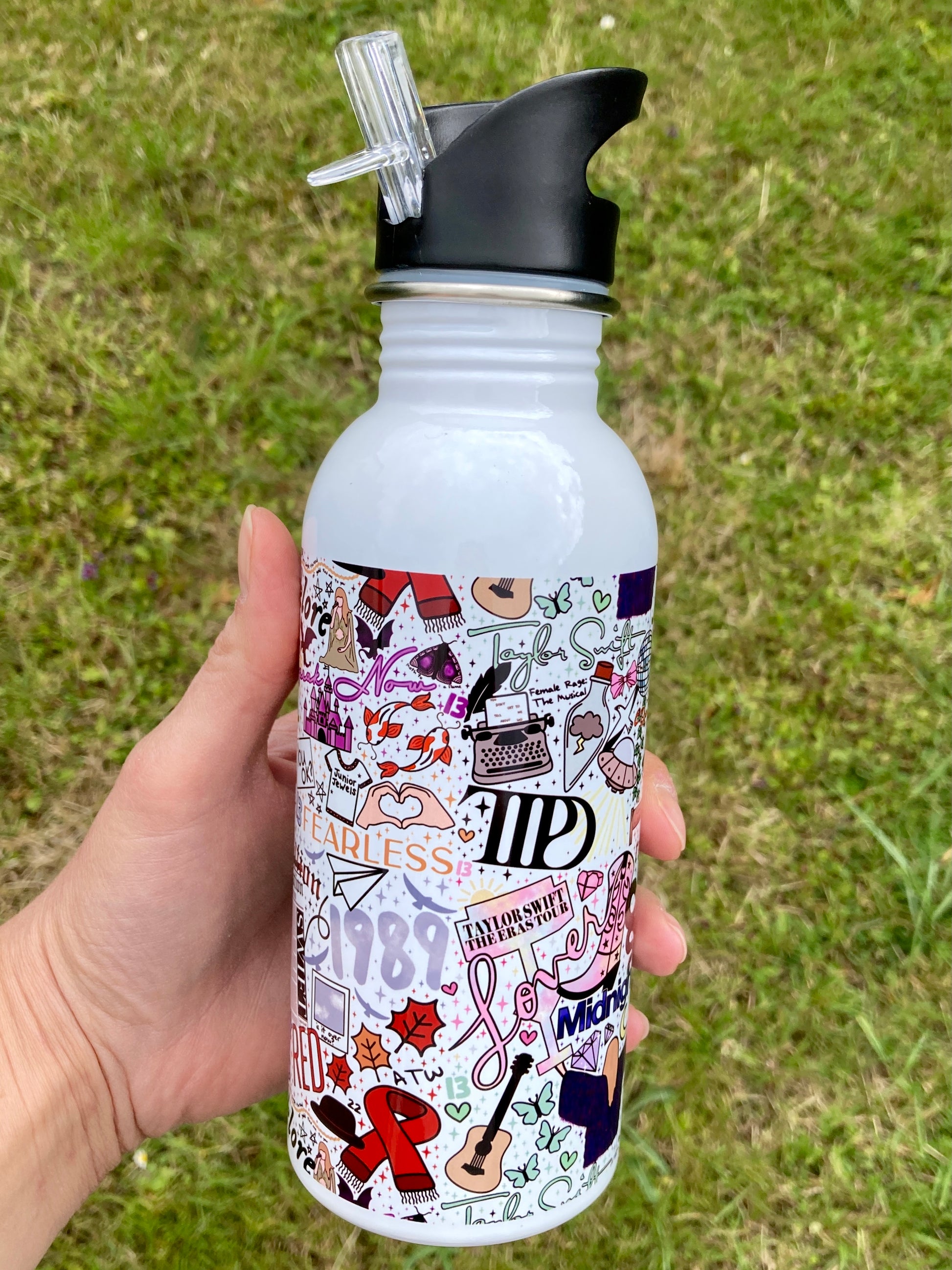 White water bottle with colorful designs held in a hand against a grassy background