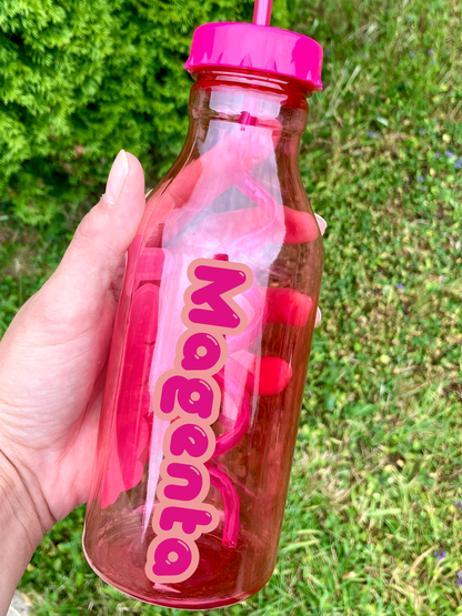 Hand holding a pink and clear 'Mogenta' water bottle with a pink cap against a grassy background.