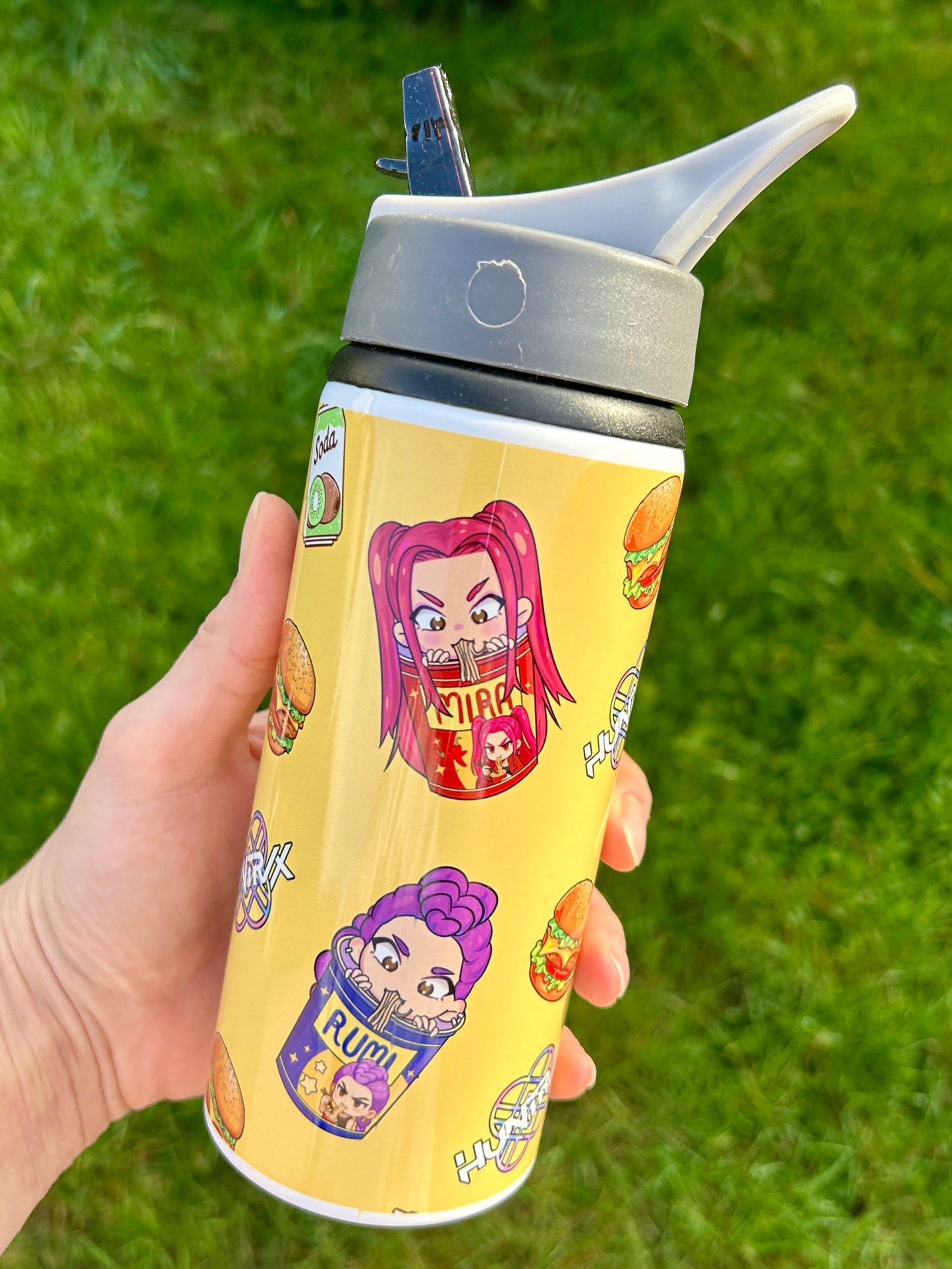 Yellow water bottle with cartoon character design held against a grass background