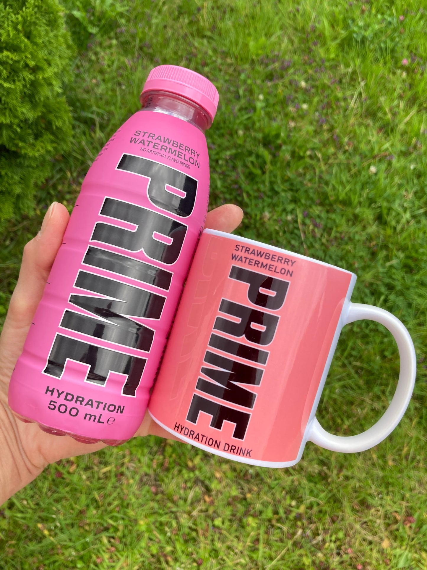 Pink 'PRIME' bottle and container held in a hand with grass background