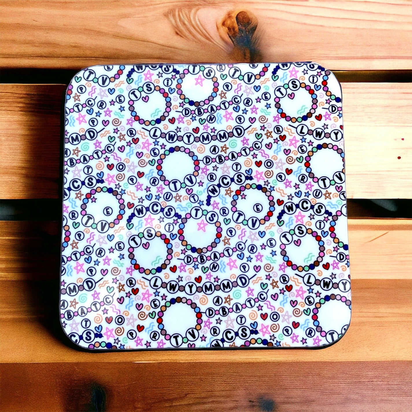 Square coaster with colorful letter and heart friendship bracelet pattern on a wooden surface