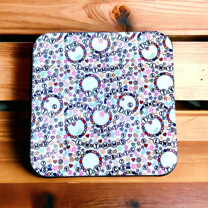 Square coaster with colorful letter and heart friendship bracelet pattern on a wooden surface